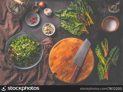 Rustic vegetarian food background with blank cutting board, knife and colorful chard leaves for vegetarian cooking. Top view. Rural cuisine style.