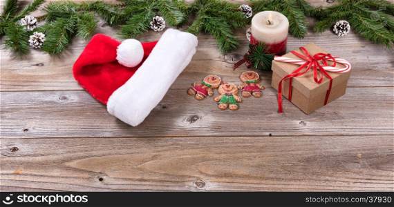 Rustic wooden boards with Christmas holiday candle, cookies, gift box, Santa cap and evergreen branches.