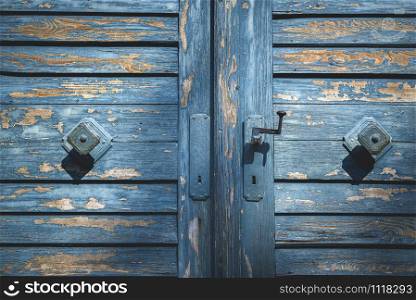 Rustic wooden door with shriveled blue paint close-up on doorknobs. Antique blue wood gate. Aged wooden door with blue paint and door handles.