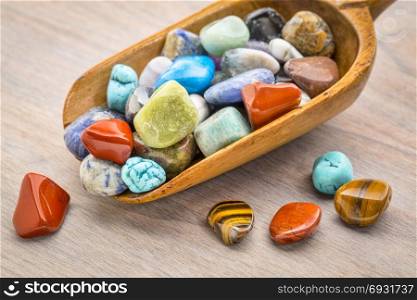 rustic wooden scoop of colorful, polished, semiprecious stone on grained wood
