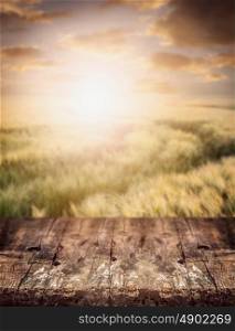 Rustic wooden table over wheat field and sunset sky, nature background.