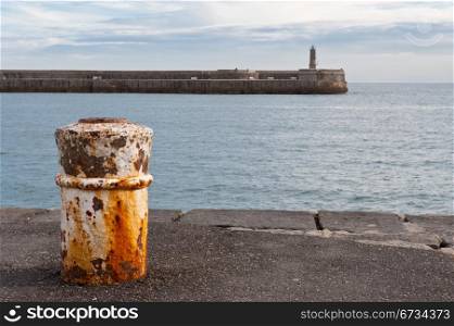 Rusty Bollard and the Old Lighthouse on the Atlantic Coast of Spain