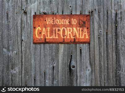 Rusty metal sign on wooden wall with the phrase: Welcome to California.