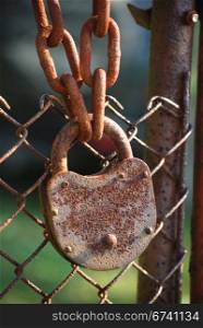 Rusty padlock, iron chain and chain-link iron fence close-up