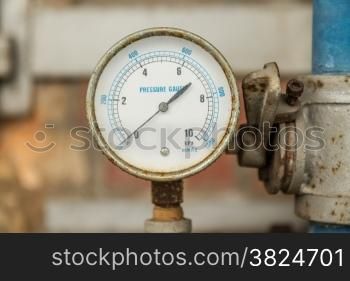 Rusty Pressure Gauge connected to pipes with brick wall behind