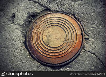 rusty round manhole on the broken asphalt