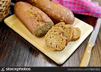 Rye baguettes on a board with a knife, a wicker basket, napkin on a dark wooden board