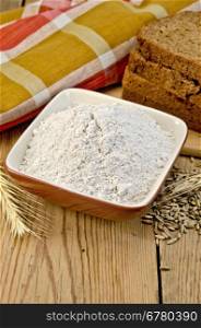 Rye flour in a bowl, homemade loaves of rye bread, spikelets and grain of rye, cloth on a background of wooden boards