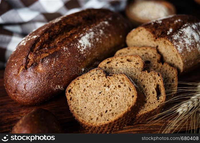 Rye homemade bread, checkered linen napkin and spikelets are on a dark wooden background