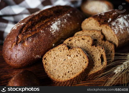 Rye homemade bread, checkered linen napkin and spikelets are on a dark wooden background