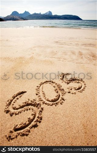 S.O.S written in the sand of an island with the ocean in the distance