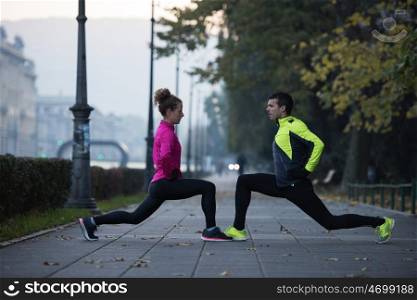 s young jogging couple warming up and stretching before morning running in the city