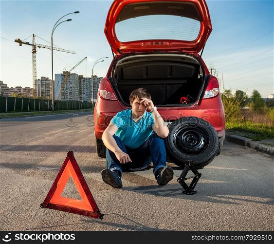 Sad and depressed man sitting near car with punctured tire