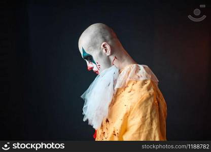 Sad bloody clown with makeup in carnival costume, side view. Crazy maniac, scary monster
