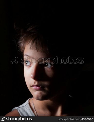 sad boy in the dark, focused light on the one side, looking away, loneliness concept
