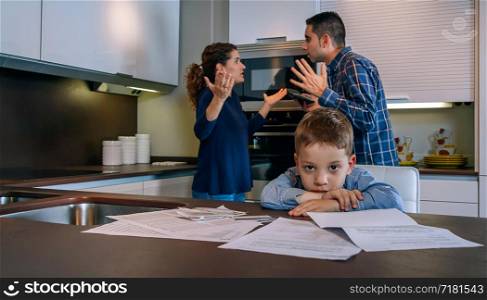 Sad boy looking at camera while his parents argue in the kitchen. Sad boy looking camera while his parents argue