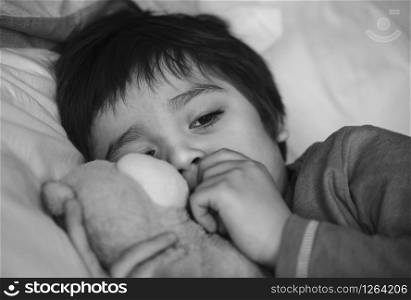 Sad boy wearing pajamas cuddle teddy bear in bed on the morning, Sad kid waking up from nightmare, Scared child waking up early morning because of bad dream, Toddler hugging teddy