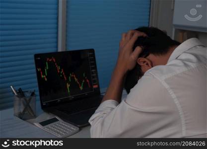Sad businessman working at night, in-front-of laptop screen showing trading graph down, bitcoin, stock market