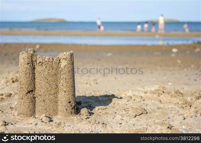 Sad castle on the beach with family playing at background