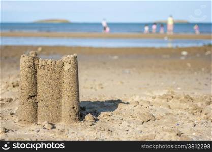 Sad castle on the beach with family playing at background