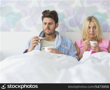 Sad couple holding coffee mugs while relaxing on bed