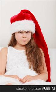 Sad cute little girl kid in red santa claus hat and white dress. Chrtistmas holiday season.. Sad little girl kid in santa claus hat. Christmas.