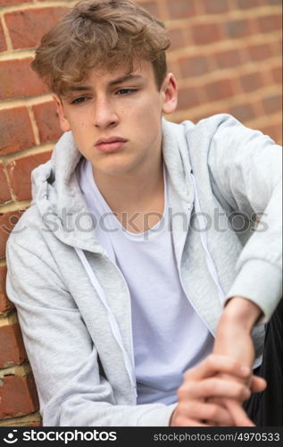 Sad depressed male boy teenager outside leaning on brick wall wearing a gray hoody