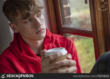 Sad depressed thoughtful teen boy male teenager young man looking out of a window drinking coffee or tea
