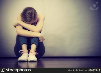 Sad depressed young teenage girl sitting by wall hiding face. School, adolescence, home violence, unwanted love problems.. Sad depressed young teenage girl sitting by wall