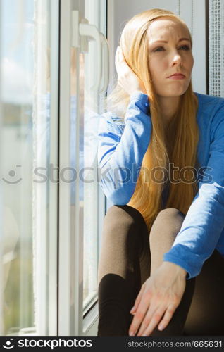 Sad depressed young teenage woman having social problems sitting on windowsill in embryonal position. Young teenage sad woman