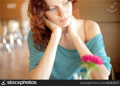 Sad despondent redhead woman seated at a table with her chin on her hand.