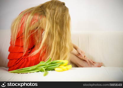 Sad elegant woman with long hair sitting on sofa being depressed, tired. Having tulip bouquet. Sad elegant woman sitting on sofa with tulip