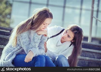 Sad Female Teen is Crying because of Teenage Problems, and Her Friend Looks Sympathetically at Her, Sitting on the Stairs