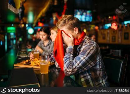 Sad football fan covers face with hands at the counter in sports bar. Tv broadcasting, favorite team loss