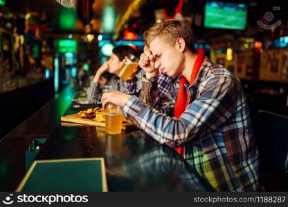 Sad football fan covers face with hands at the counter in sports bar. Tv broadcasting, favorite team loss. Sad fan covers face with hands in sports bar