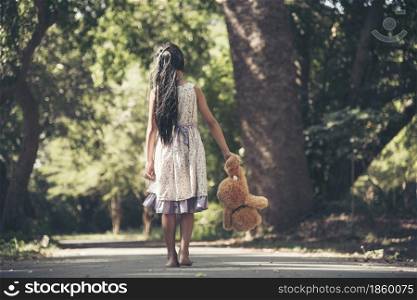 Sad girl hugging teddy bear sadness alone in green garden park. Lonely girl feeling sad unhappy walking outdoors with best friend toy. Autism child play teddy bear best friend. Family violence concept