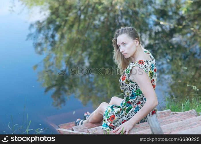 sad girl on the river bank, beautiful adult woman sitting on the riverbank concept expecting sadness