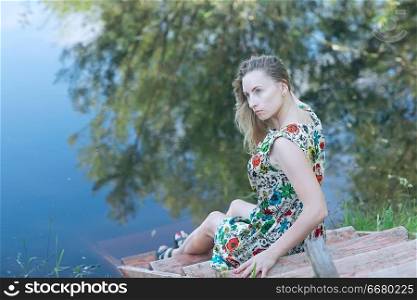 sad girl on the river bank, beautiful adult woman sitting on the riverbank concept expecting sadness