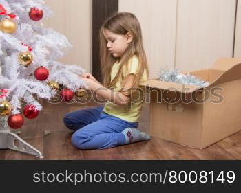 Sad girl removes a Christmas tree with toys. Sad five year old girl takes a toy artificial Christmas tree