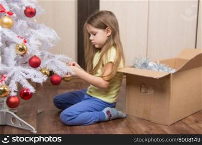 Sad girl removes a Christmas tree with toys. Sad five year old girl takes a toy artificial Christmas tree