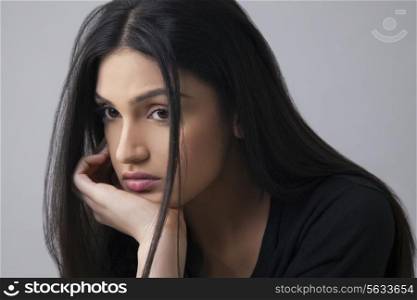 Sad Indian young woman looking away with hand on chin over colored background