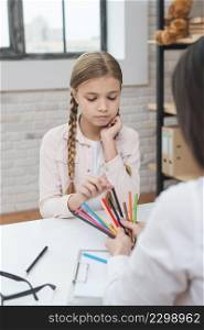 sad little girl choosing colored pencils hold by female psychologist