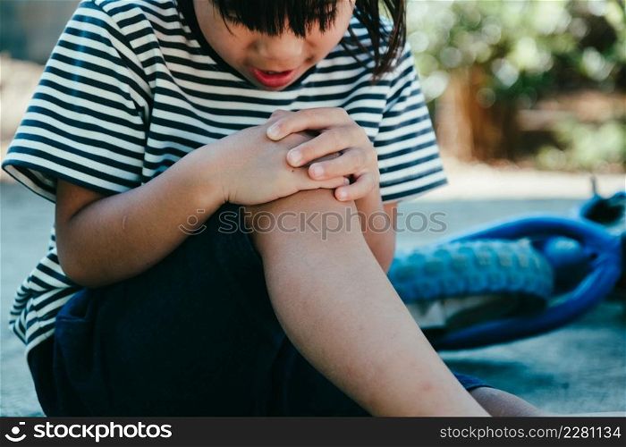 Sad little girl sitting on the ground after falling off her bike at summer park. Child was injured while riding a bicycle.
