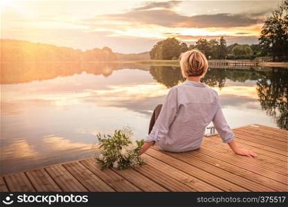 Sad lonely beautiful woman with bunch of flower sitting on the pier with copy space