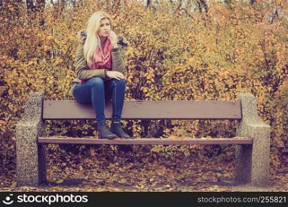 Sad looking woman relaxing sitting on bench in park during autumn weather.. Woman relaxing sitting on bench in autumnal park
