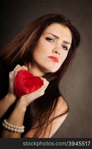 Sad lovely woman holds red heart on black. Woman brunette long hair girl wearing black dress holding red heart love symbol studio shot on dark. Heartbroken young female. Sad unhappy face expression