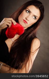 Sad lovely woman holds red heart on black. Woman brunette long hair girl wearing black dress holding red heart love symbol studio shot on dark. Heartbroken young female. Sad unhappy face expression