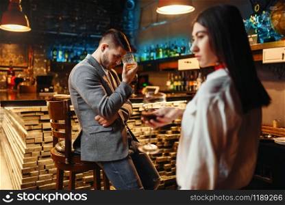 Sad man and woman in a bar, husband and wife relaxing together in nightclub. Man lovingly looks on woman at wooden bar counter