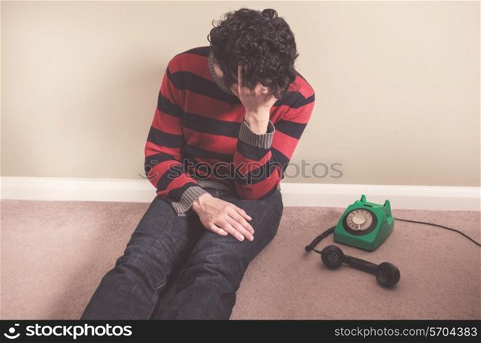 Sad man sitting on the floor has received bad news on the telephone