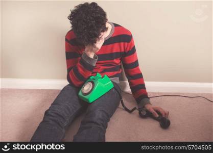Sad man sitting on the floor has received bad news on the telephone